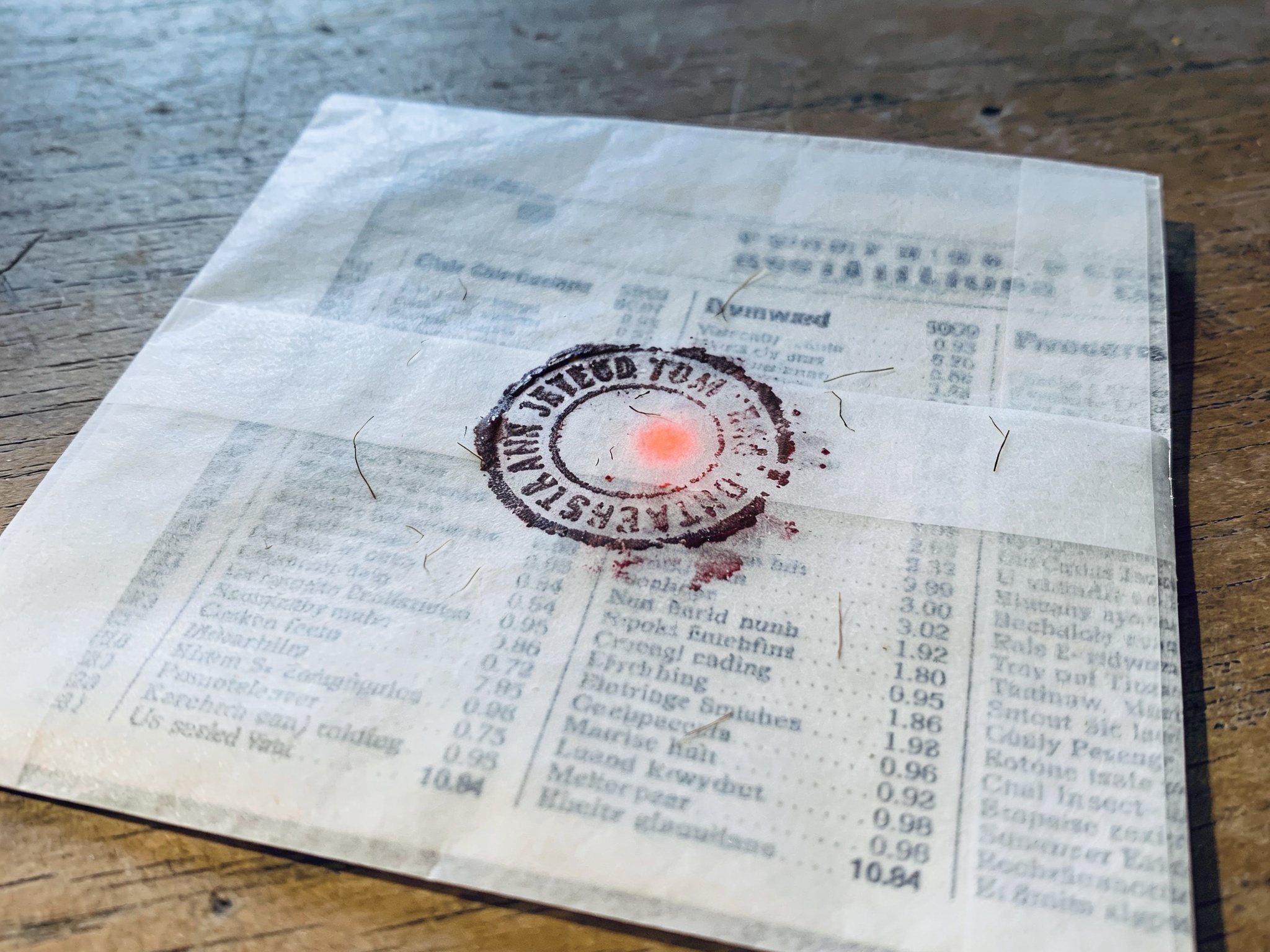 Smudged circular stamp on translucent paper over a blurred classified ad page.